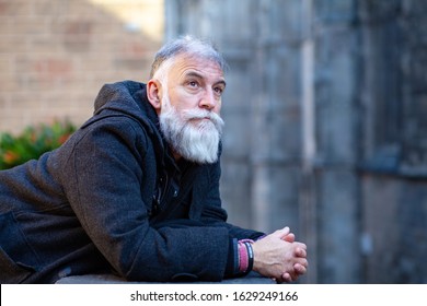 Older Man With White Beard And Black Hat Talking On The Phone In The Middle Of The Street