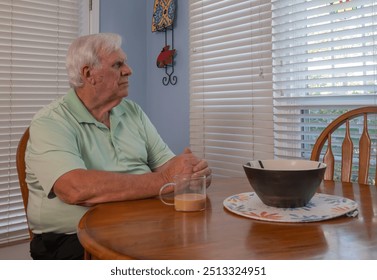 Older man with white hair wearing a green shirt looks out the window while enjoying his coffee. He smiles and seems to enjoy the scenery. - Powered by Shutterstock