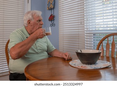 Older man with white hair wearing a green shirt looks out the window while enjoying his coffee. He smiles and seems to enjoy the scenery. - Powered by Shutterstock