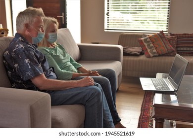 An Older Man And Woman Wearing Masks Sit Together On A Sofa With A Laptop In Front Of Them Talking To Family On A Video Call