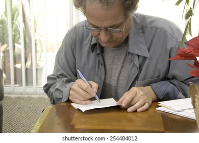 Older Man Writing Checks/Senior Paying Bills/Senior Working In The Early Afternoon On His Finances