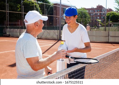 Older Man And Young Man Talking On Court Playing Tennis