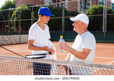 Older Man And Young Man Talking On Court Playing Tennis