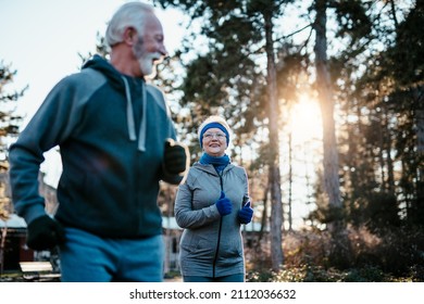 An Older Married Couple Enjoys Exercising And Jogging On A Beautiful Sunny Winter Day.