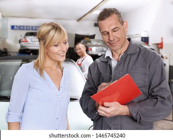 The older master of the car workshop with grey hair and overall tell something to the attractive blonde female customer about her car in the garage - Powered by Shutterstock