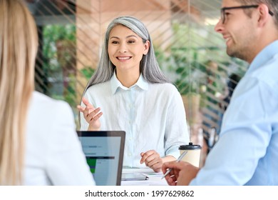 Older Mature Asian Business Woman Training Young Interns Trainees Explaining Sharing Professional Skills At Group Meeting In Modern Office. Mid Age Senior Teacher With Group Of Students On Seminar.