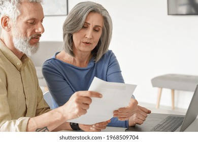Older Mature Couple Checking Bank Documents Using Laptop At Home. Senior Mid Age Retired Man And Woman Reading Paper Bills, Calculating Pension Or Taxes, Planning Retirement Finances, Doing Paperwork.