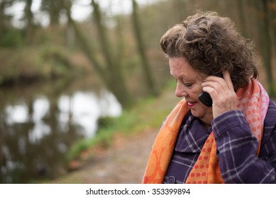 Older, Mature Woman. Calling On A Cell Phone While Being Outdoors. Nature. Bad News Call. Sad.