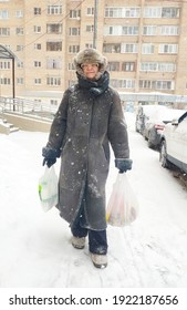 Older Mature Woman Carries Shopping Bags In A Heavy Snowfall. Middle Aged Grandmother walking Out Of The Store In A Blizzard. The Concept Of Bad Weather In The City