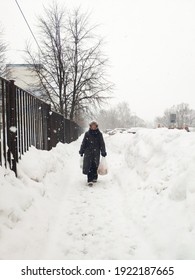 Older Mature Woman Carries Shopping Bags In A Heavy Snowfall. Middle Aged Grandmother walking Out Of The Store In A Blizzard. The Concept Of Bad Weather In The City