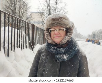 Older Mature Woman Carries Shopping Bags In A Heavy Snowfall. Middle Aged Grandmother walking Out Of The Store In A Blizzard. The Concept Of Bad Weather In The City