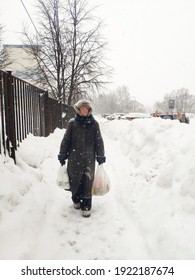 Older Mature Woman Carries Shopping Bags In A Heavy Snowfall. Middle Aged Grandmother walking Out Of The Store In A Blizzard. The Concept Of Bad Weather In The City