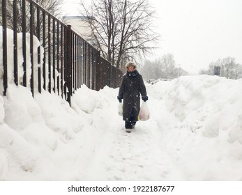 Older Mature Woman Carries Shopping Bags In A Heavy Snowfall. Middle Aged Grandmother walking Out Of The Store In A Blizzard. The Concept Of Bad Weather In The City