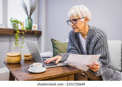 An Older Mature Woman In Her 60s Is Sitting In The Living Room, Holding A Sheet Of Paper, Reading A Letter, Checking Notification Rates, Paying Bills, Using An Online E-banking App.