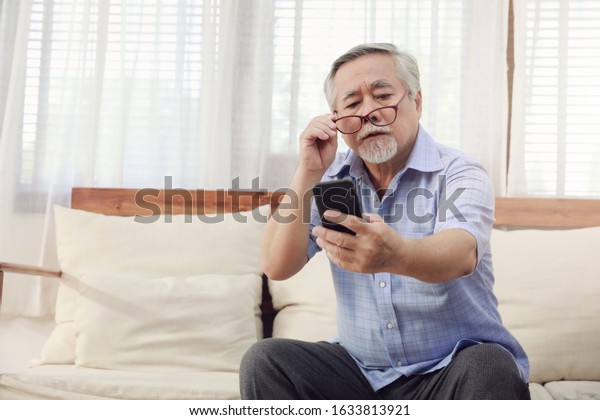 Older men move glasses down to look at the\
phone in the hand due to Hyperopia problems, which makes vision\
difficult.Health problems of the\
elderly.
