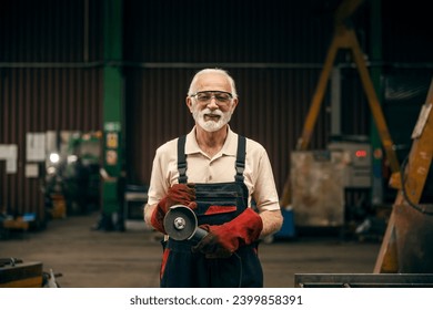 An older metallurgy worker is posing with grinder at factory and smiling at the camera. - Powered by Shutterstock