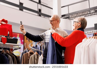 Older people taking pictures in store, comparing blazers on racks with items listed online on app. Senior couple shopping for formal attire during christmas season, looking for festive clothes. - Powered by Shutterstock