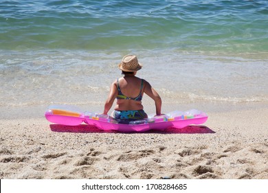 Older Plus-size Woman Sitting On A Beach On Pink Air Mattress. 