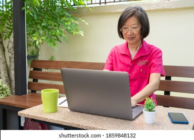 Older Retired Asian Woman Using Computer To Write Email And Sitting At Home