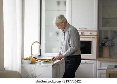 Older Retired Homeowner Man Cooking Salad In Modern Kitchen, Chopping Fresh Vegetables On Board, Preparing Organic Meal For Dinner From Natural Ingredients. Healthy Eating, Elderly Ag