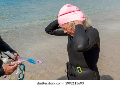 Older Retired Woman In Wetsuit Putting On Swimming Cap