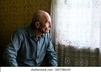 older sad bald man siting on sofa in village house and looking to window senior persons concept