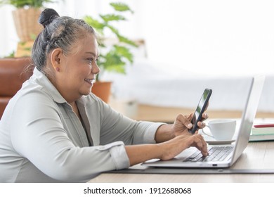 An Older Senior Asian Woman Holding Smartphone And Using Tablet Notebook Computer.