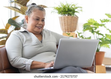 An Older Senior Asian Woman Sitting On Sofa And Using Notebook Labtop Computer In Living Room With Happy Face. Idea For Older People Learning New Skill Technology