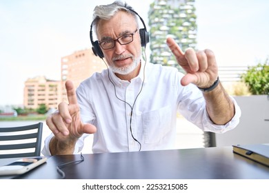 Older senior business man, online teacher or coach wearing headphones talking to webcam teaching virtual class, leading remote hybrid call meeting or consulting client. Web camera view shot - Powered by Shutterstock