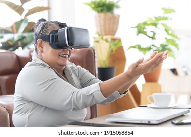 An older senior grey hair Asian woman wearing VR mask and rise hand in the air look like playing game with fun and joy. - Powered by Shutterstock