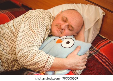 Older Senior Man Sleep In Pajamas With Toy Owl Pillow In Bedroom At Cozy Place