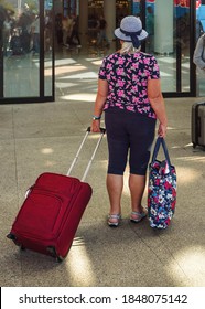 Older Senior Woman In Summer Holiday Clothes Pulling Her Luggage Entering Airport Terminal, View From Behind