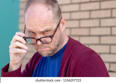 Older Serious Middle Aged Dad Man Wearing A Cardigan Looking Down His Nose Over His Glasses Making Eye Contact Directly At Camera, Disapproval Judgement Concept, Horizontal Shot