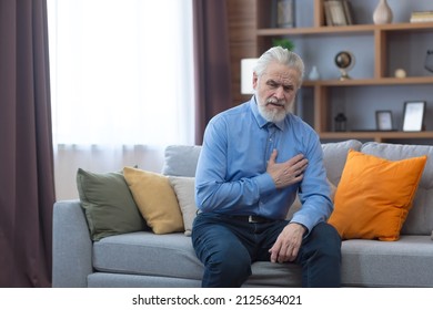 Older Single Man Alone At Home, Sitting On Sofa, Holding Hands On Chest, Has Severe Chest Pain