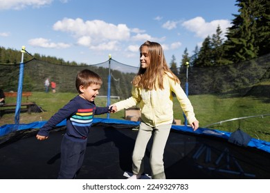 Older sister and her little brother are jumping together on a netted trampoline in the backyard - Powered by Shutterstock