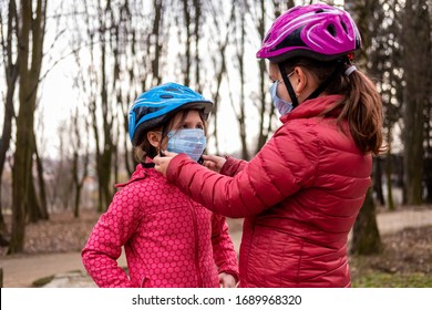 The older sister puts on the younger one a medical mask before riding a Bicycle. The concept of protection FROM covid-19 coronavirus infections.