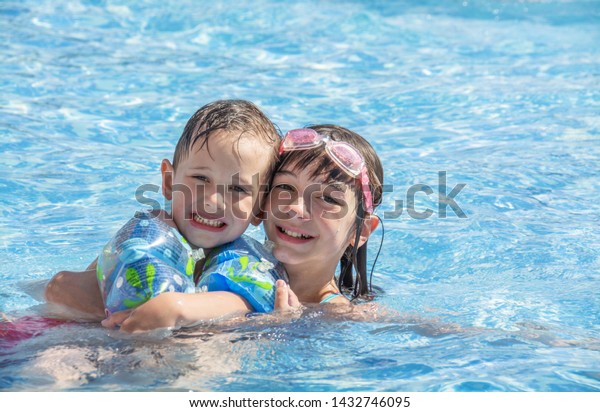 Older sister and younger brother swim in the outdoor\
children\'s pool