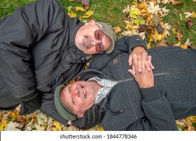 Older White Gay Male Couple Playing In The Autumn Leaves.