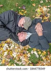 Older White Gay Male Couple Playing In The Autumn Leaves.