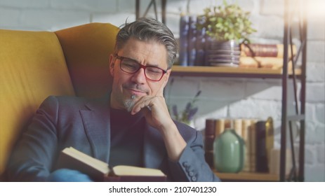 Older white man in glasses reading book at home sitting in armchair in cosy room. - Powered by Shutterstock