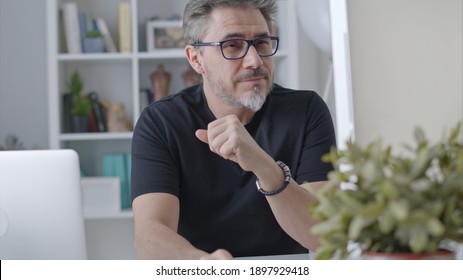 Older White Man In Glasses Sitting At Desk Using Desktop Computer In Home Office. 50s Businessman Staying Home In Casual Working Online Thinking On Business Solution, Smiling.