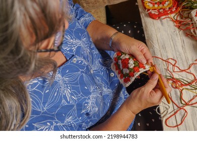 Older White-haired Woman Crocheting On The Armchair At Home