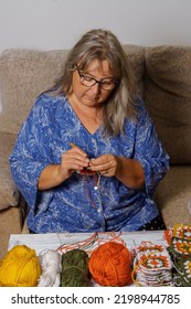 Older White-haired Woman Crocheting On The Armchair At Home