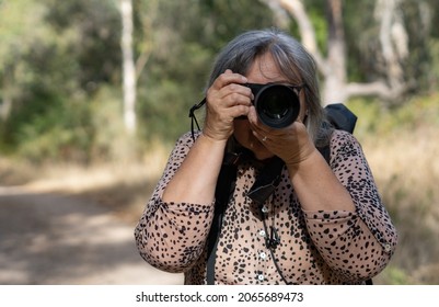 Older White-haired Woman Taking Pictures In The Forest