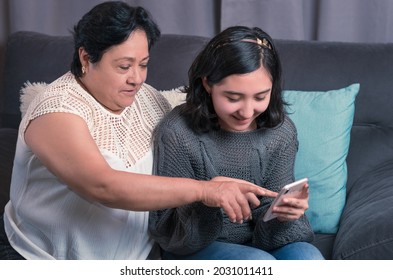 older woman 60 year old latin grandmother using cell phone and having fun with her granddaughter taking photos and watching videos