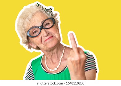 An Older Woman With An Angry Facial Expression Shows Fuck You. Isolated The Concept Of Discontent And Protest Of Old Woman . Yellow Background, Stroke.