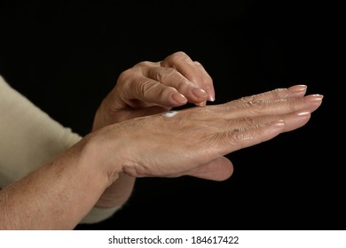 Older Woman Applying Cream On Hands Closeup On Black Background