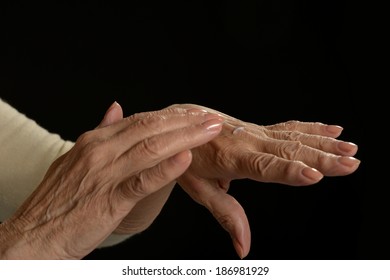 Older Woman Applying Cream On Hands Closeup On Black Background