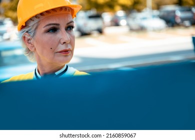 Older Woman Architect Controlling Construction Site. Elderly Female Civil Engineer With Yellow Hardhat And Reflective Vest Checking New Buildings. Senior Woman Supervisor With Blueprint. Copy Space