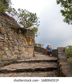 An Older Woman Ascending A Stone Stairway With A Staff And Heavy Backpack.  Perhaps She Is A Pilgrim Or Maybe She Is Just Carrying Groceries To Her Mountain Home Near Bogota, Columbia